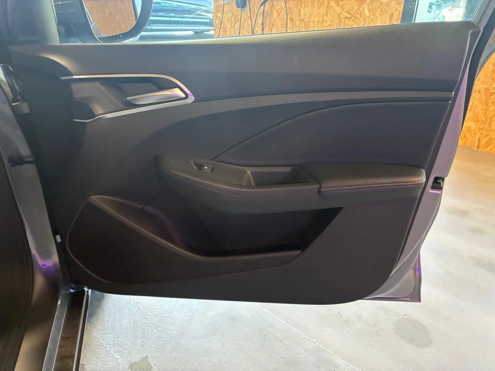 Vue intérieure de la porte avant gauche noire du MG3 1.5 HYBRID+ 195 LUXURY avec poignée argentée et accoudoir rembourré.