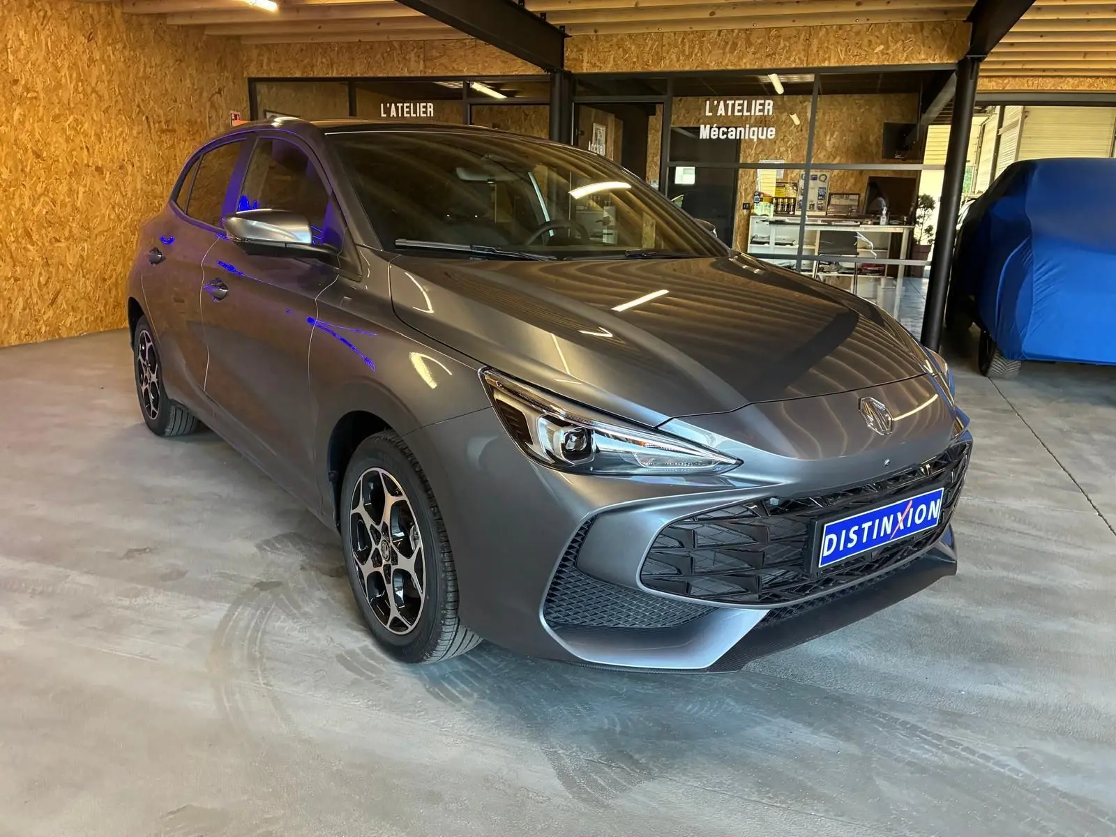 Vue 3/4 avant d'une MG3 1.5 Hybrid+ 195 Luxury gris métallisé, avec jantes noires et détails sportifs visibles.