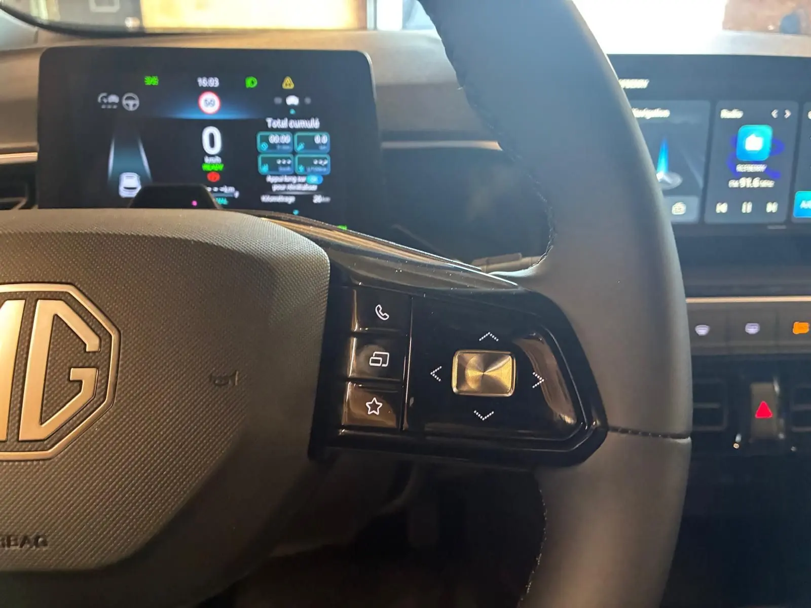 Gros plan sur le volant noir du MG3 1.5 HYBRID+ 195 LUXURY avec commandes intégrées et tableau de bord digital en arrière-plan.