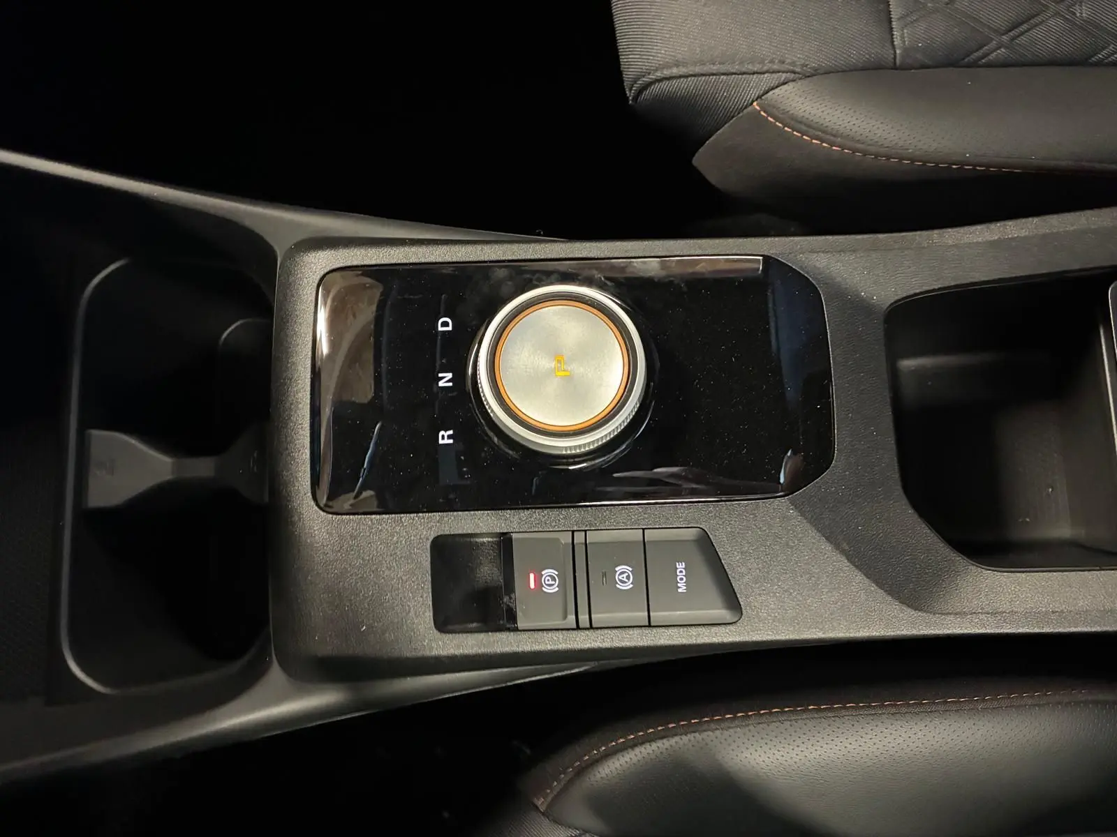 Gros plan sur la console centrale noire du MG3 1.5 HYBRID+ 195 LUXURY avec molette de sélection de vitesse et boutons de frein à main électronique.