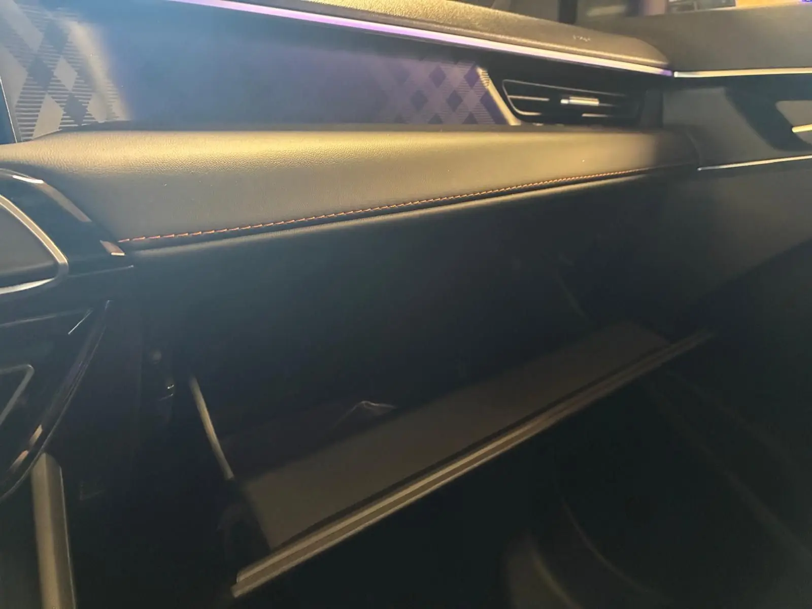 Intérieur de la MG3 1.5 HYBRID+ 195 LUXURY noir, vue côté passager sur la boîte à gants ouverte et tableau de bord cuir.