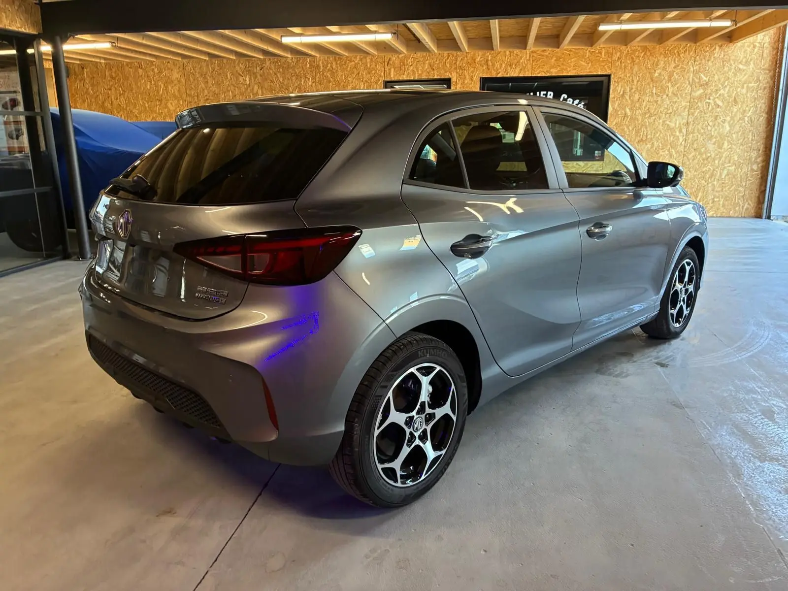 Vue 3/4 arrière droite d'une MG3 noire 2026 hybride, avec jantes alliage et vitres teintées dans un garage.