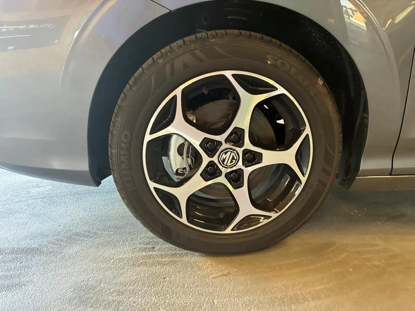 Gros plan sur la roue avant gauche noire d’une MG3 1.5 HYBRID+ 195 LUXURY avec jante alliage bicolore et logo MG central.