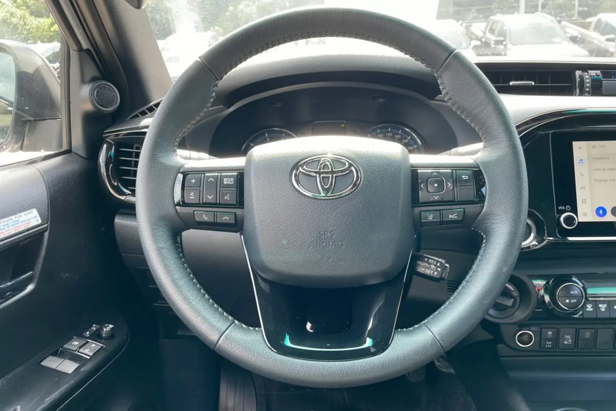 Vue intérieure centrée sur le volant noir du Toyota Hilux 4x4 blanc 2025, avec commandes intégrées et tableau de bord visible.
