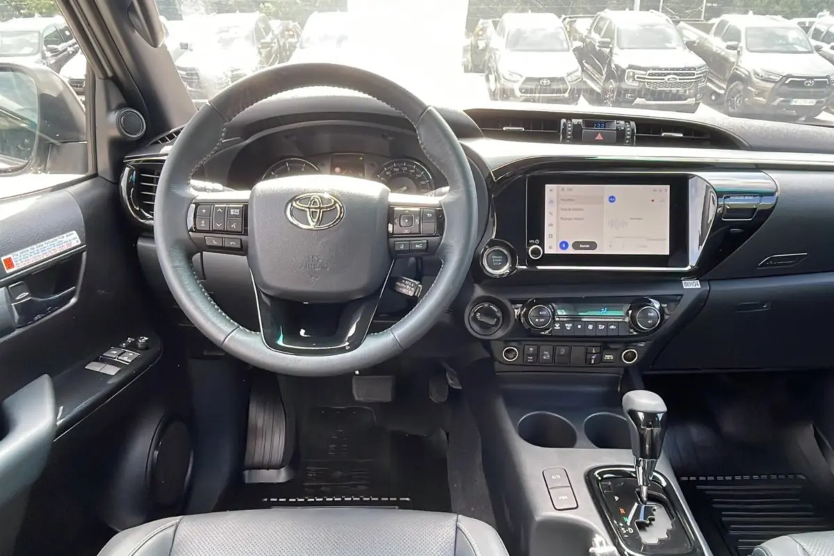 Intérieur du Toyota Hilux 2025 blanc, vue du poste de conduite avec volant multifonction et écran tactile central.