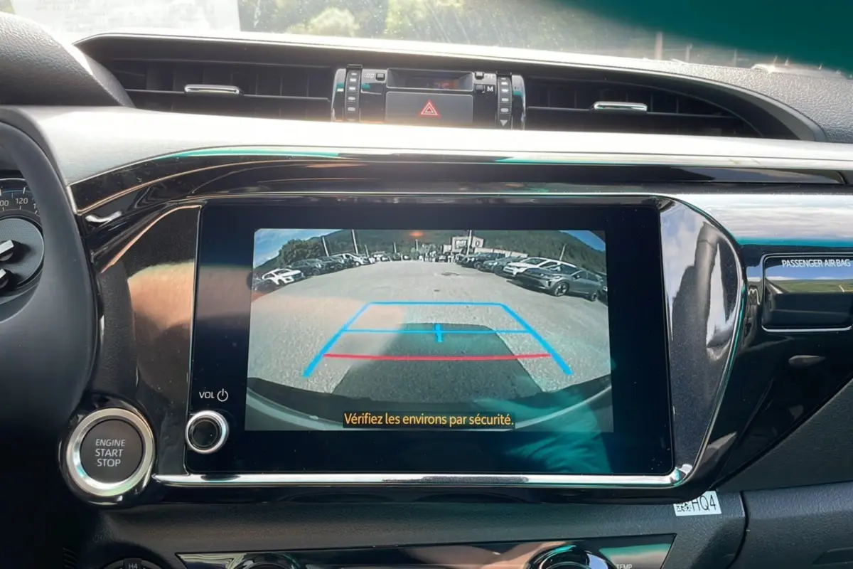 Vue intérieure du tableau de bord du Toyota Hilux 2025 blanc, écran multimédia affichant la caméra de recul avec repères colorés.