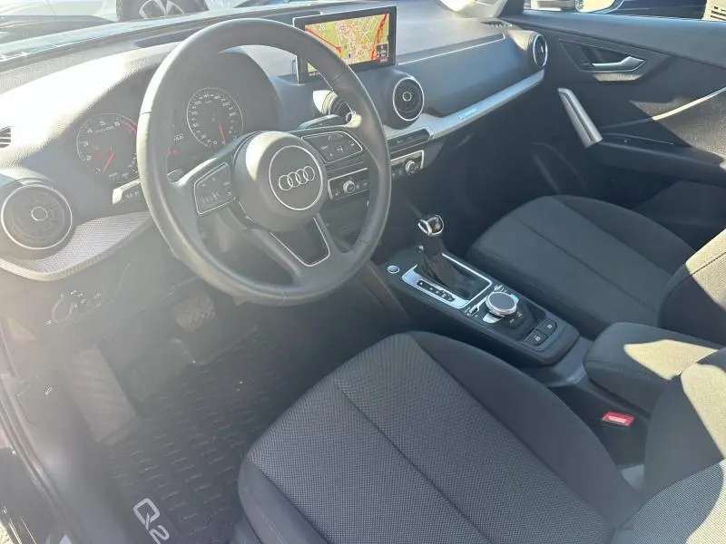 Intérieur de l'Audi Q2 35 TFSI 2023 vu côté conducteur, avec tableau de bord noir et écran de navigation allumé.