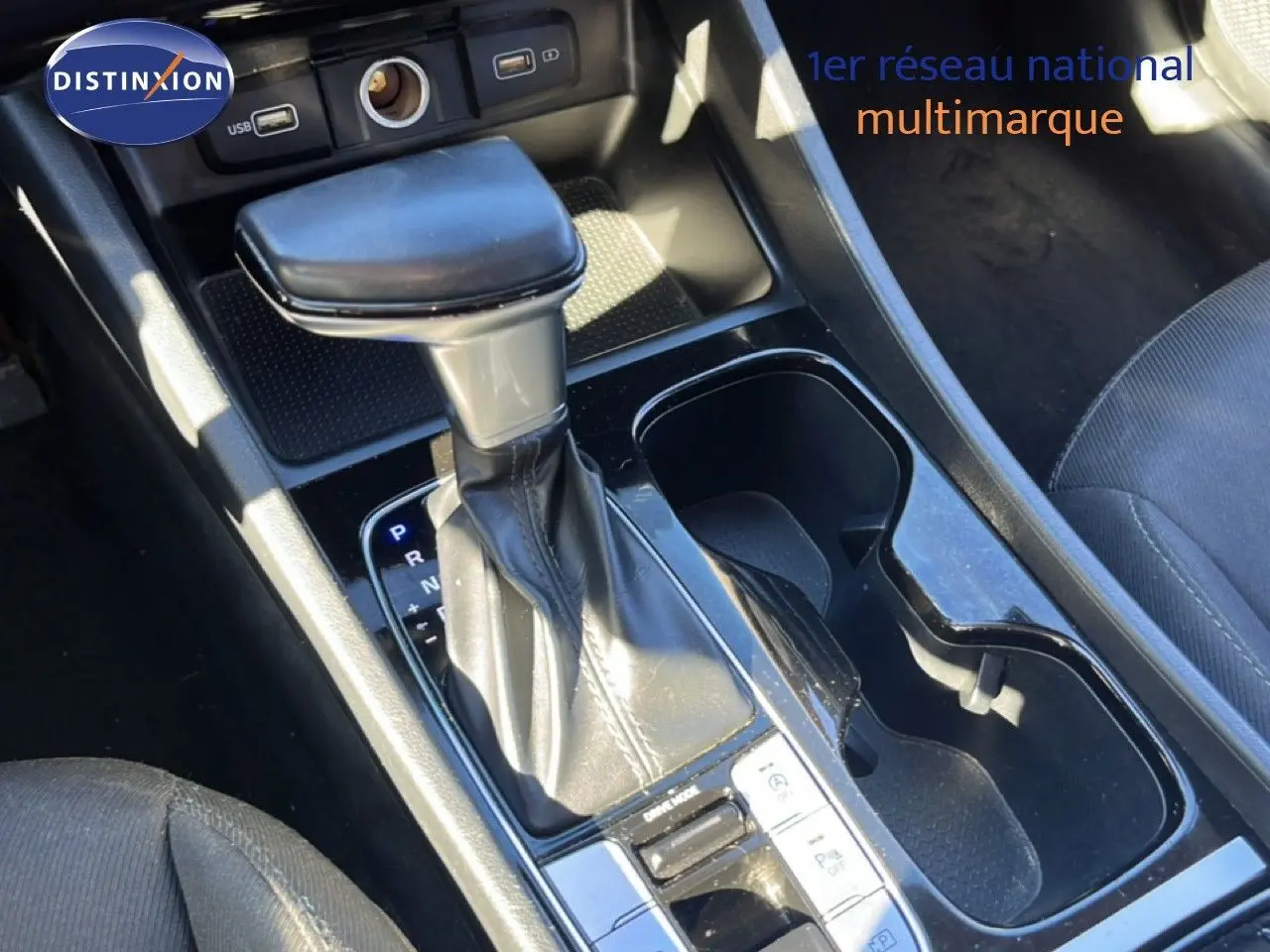 Gros plan sur le levier de vitesses automatique du Hyundai Tucson gris foncé, avec porte-gobelets et prises USB visibles.