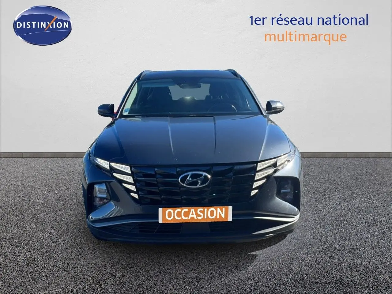 Vue avant d’un Hyundai Tucson gris foncé métal, avec calandre noire et feux LED distinctifs allumés.