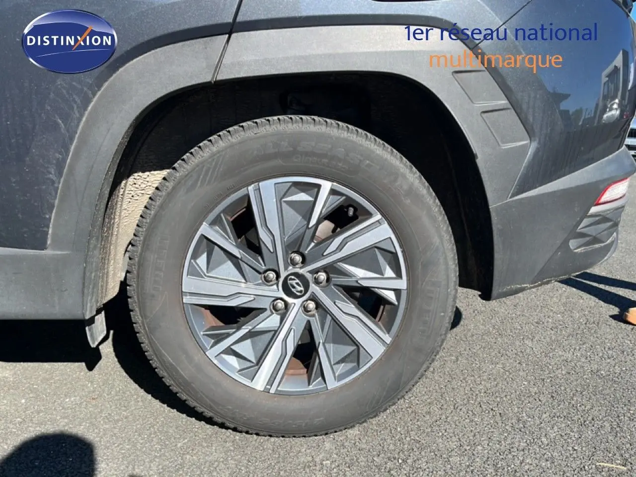 Gros plan sur la roue arrière droite d’un Hyundai Tucson gris foncé métal avec jante alliage au design géométrique.