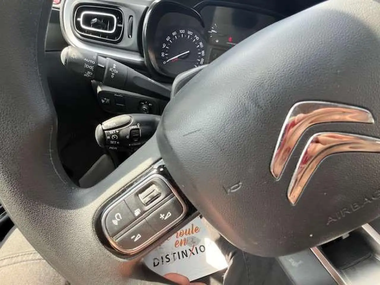 Gros plan sur le volant noir de la Citroën C3 2023 avec commandes audio intégrées et tableau de bord visible en arrière-plan.