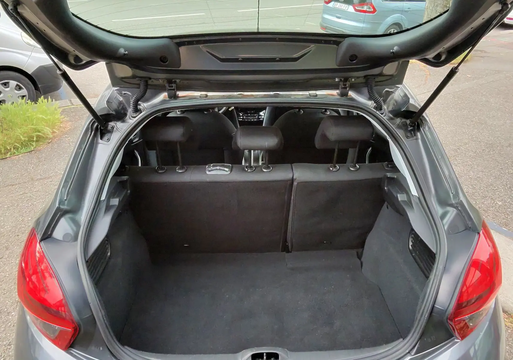 Vue arrière ouverte du coffre d'une Peugeot 208 gris foncé métal, montrant l'intérieur vide et les sièges arrière.
