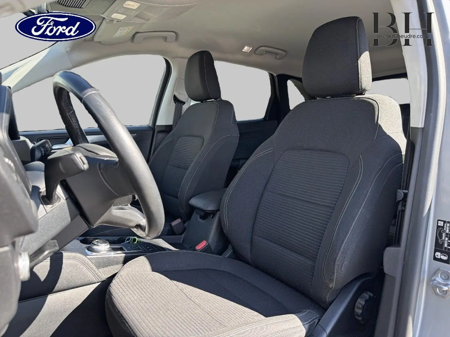 Vue intérieure côté conducteur du Ford Kuga 2.5 Duratec gris Solar, sièges tissu noir avec volant cuir multifonction.