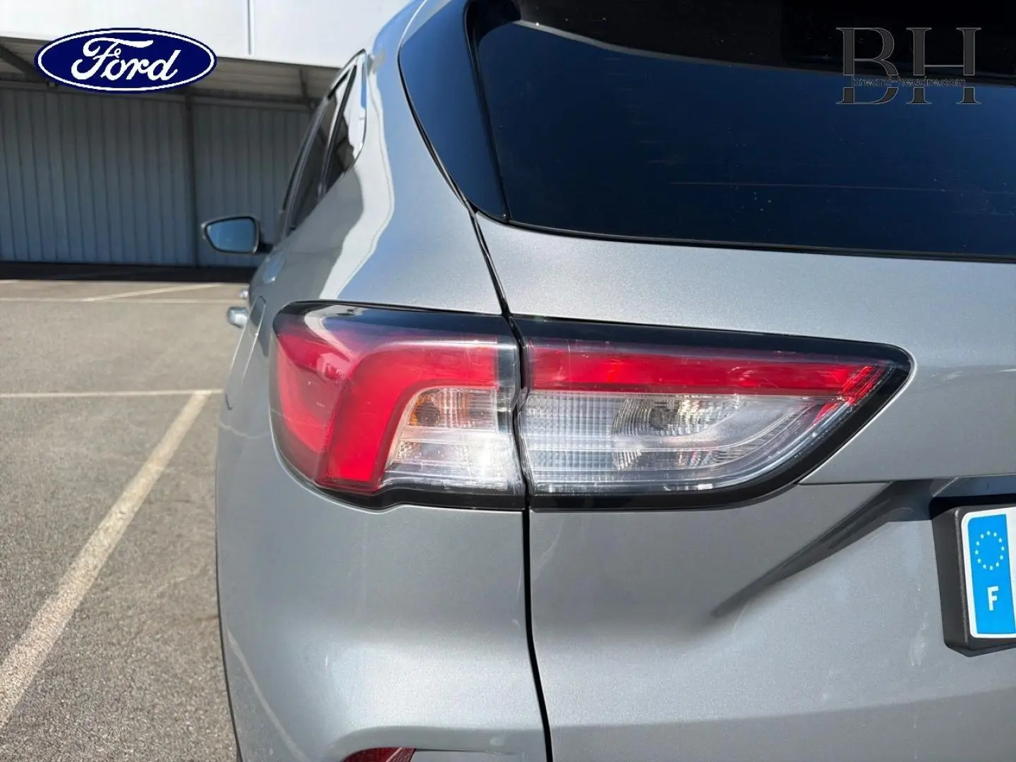 Gros plan sur le feu arrière gauche d’un Ford Kuga gris Solar métallisé, avec vitre arrière surteintée visible.