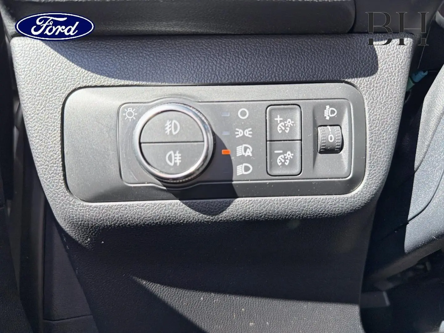 Gros plan sur les commandes d’éclairage intérieures du Ford Kuga 2021, avec molette et boutons noirs sur tableau de bord gris.