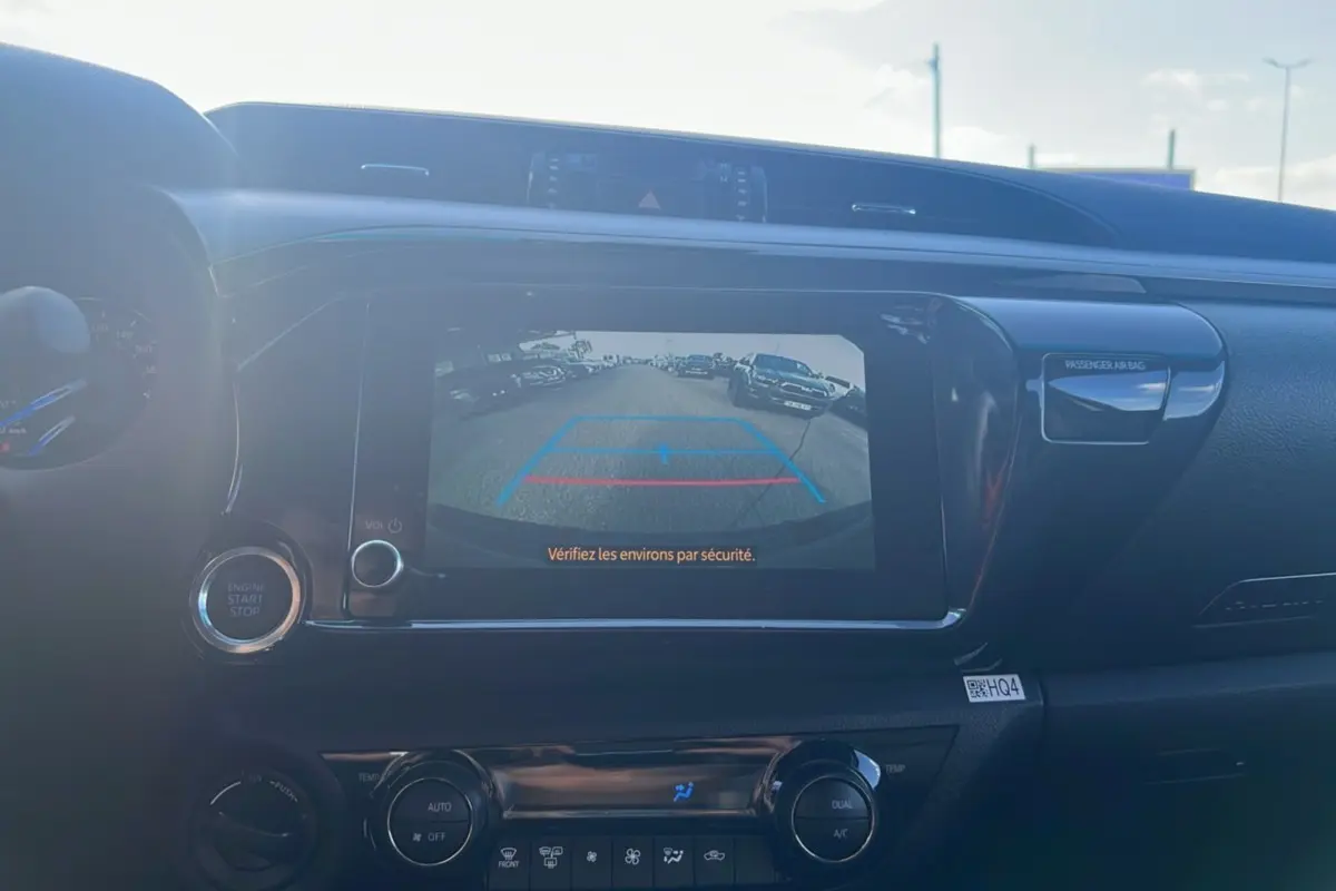 Vue intérieure du tableau de bord du Toyota Hilux 2025 avec écran de caméra de recul et commandes climatisation visibles.
