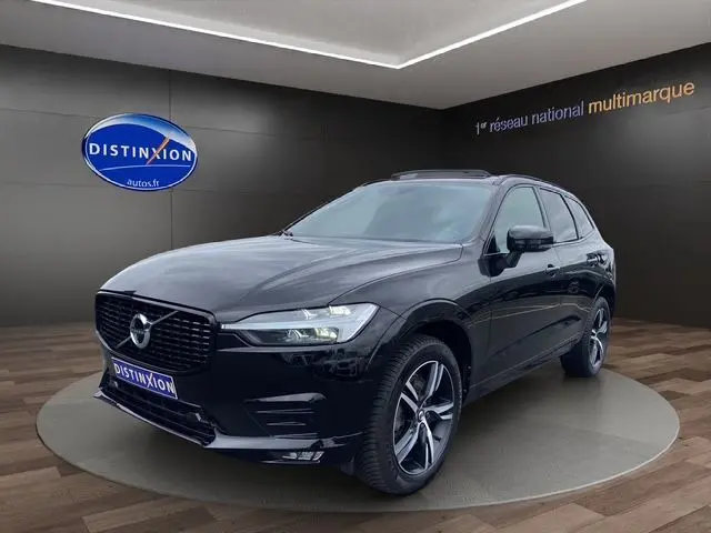 Volvo XC60 noir en 3/4 avant droit, avec toit panoramique et jantes alliage visibles dans un showroom.