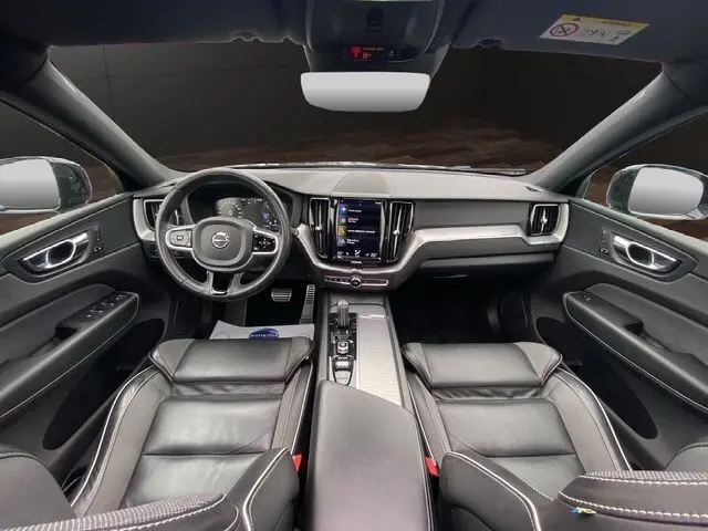 Vue intérieure avant du Volvo XC60 noir 2021, avec tableau de bord moderne, écran tactile central et sièges cuir noirs.