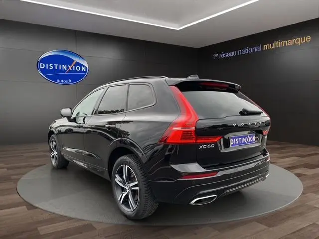 Volvo XC60 noir vue 3/4 arrière droit, avec feux arrière en L et double sortie d’échappement chromée.
