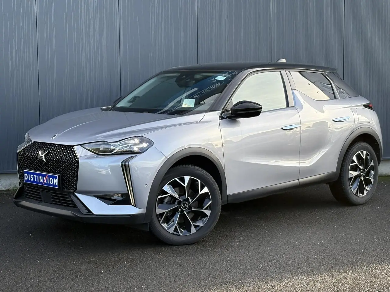 DS3 2024 gris Artense avec toit noir, vue 3/4 avant droit, calandre noire brillante et jantes alliage 18 pouces.