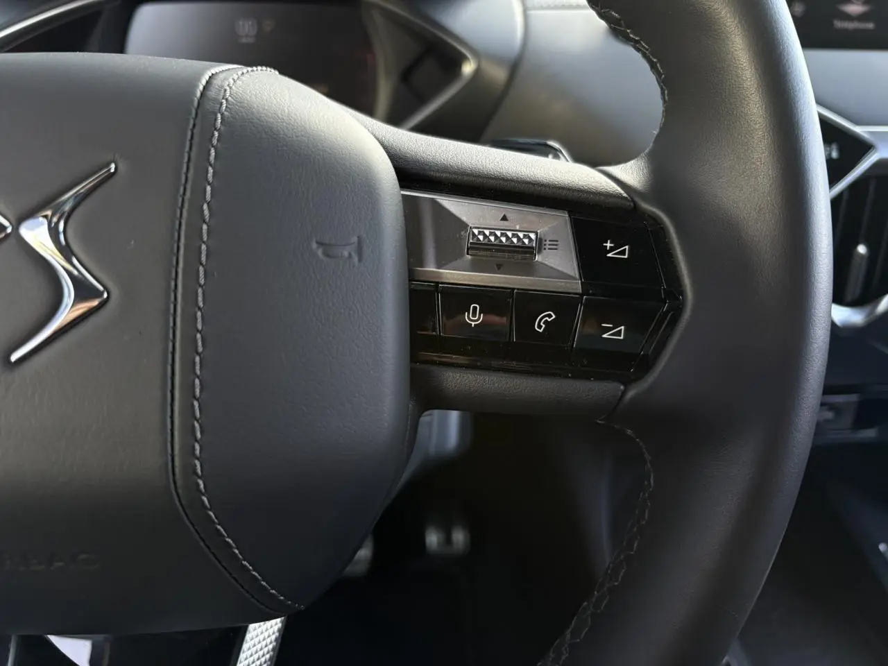 Gros plan sur le volant cuir noir du DS3 2024, avec commandes intégrées et logo DS chromé visible.