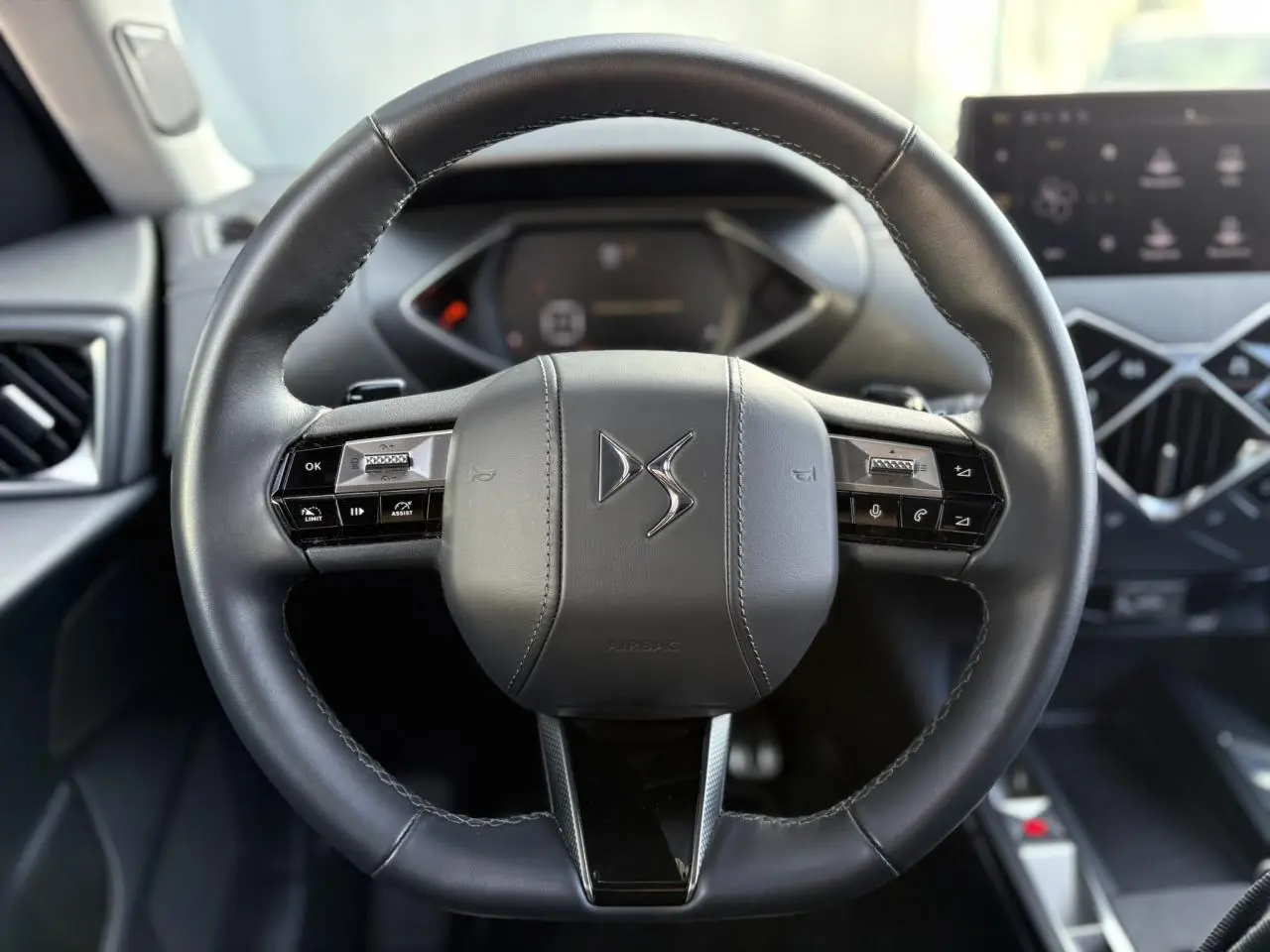 Volant cuir noir DS3 2024 avec commandes intégrées, tableau de bord numérique et écran tactile en arrière-plan.