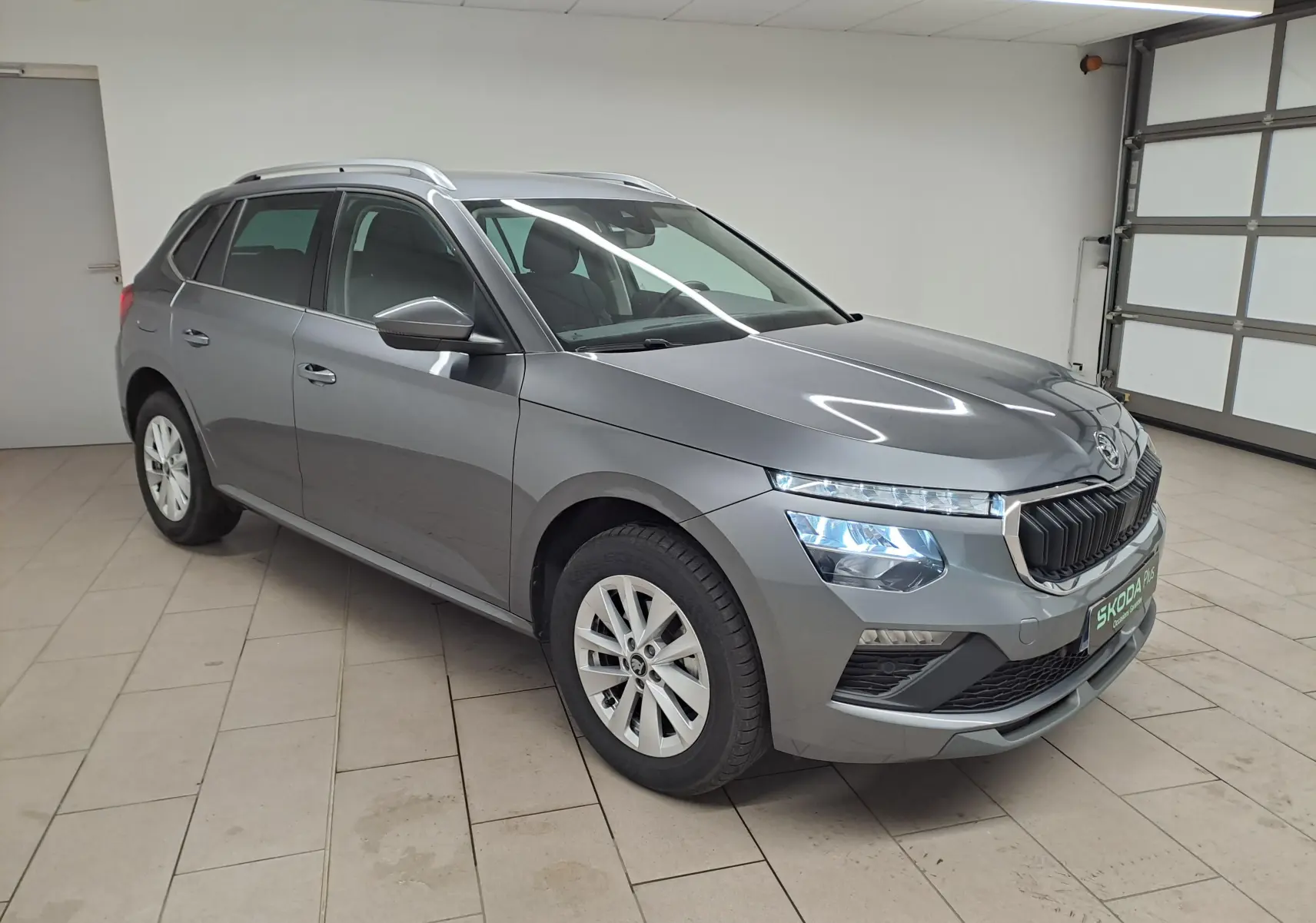 Vue 3/4 avant droite du Skoda Kamiq 2025 gris graphite métallisé avec calandre noire et feux LED allumés en intérieur.