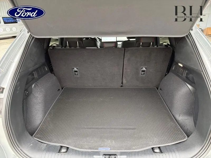 Coffre ouvert du Ford Kuga gris Solar Métallisé, vue arrière montrant la banquette arrière et tapis de coffre réversible.