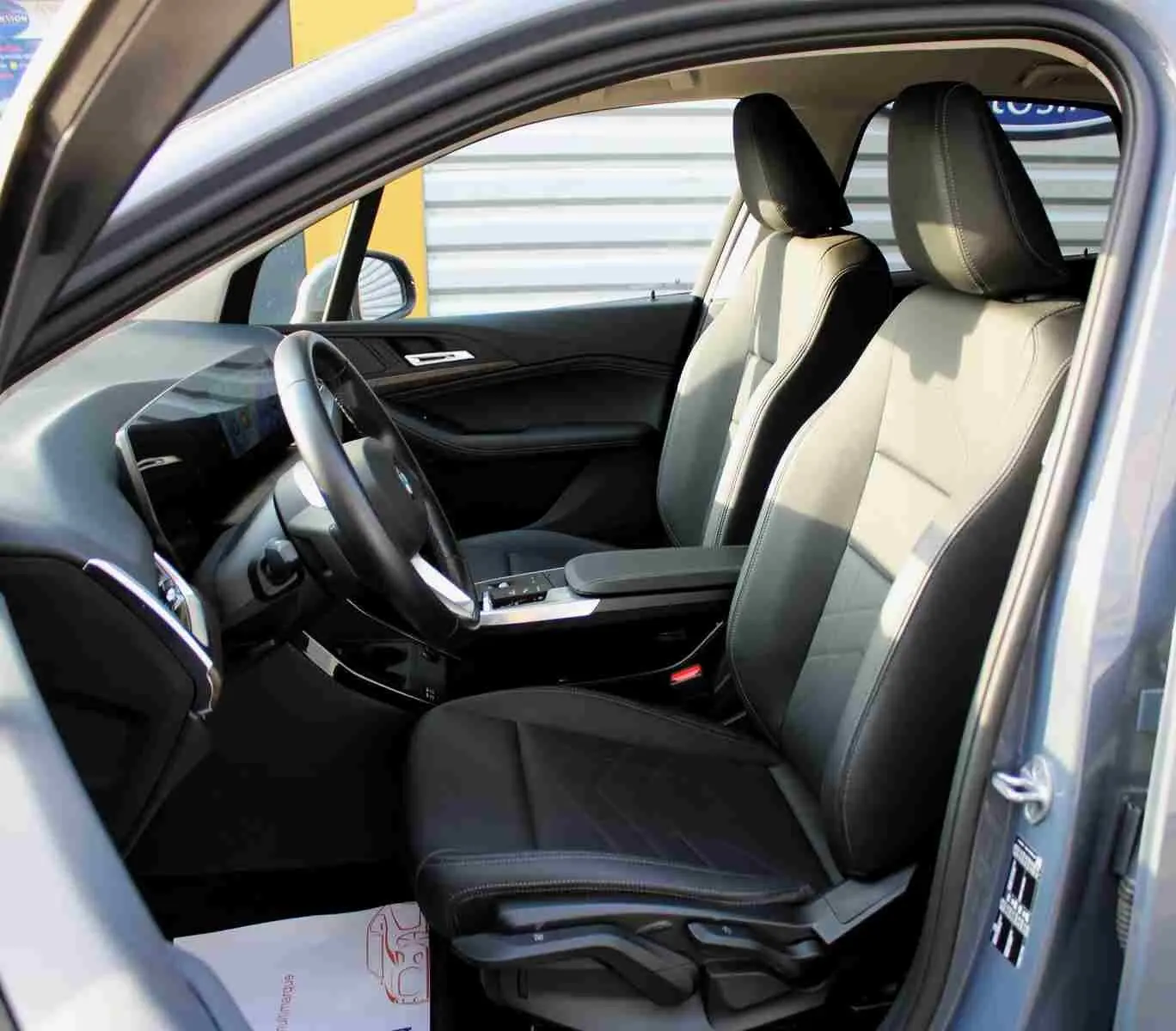 Vue intérieure côté conducteur de la BMW Série 2 Active Tourer gris Nardo, sièges cuir noir et tableau de bord moderne.