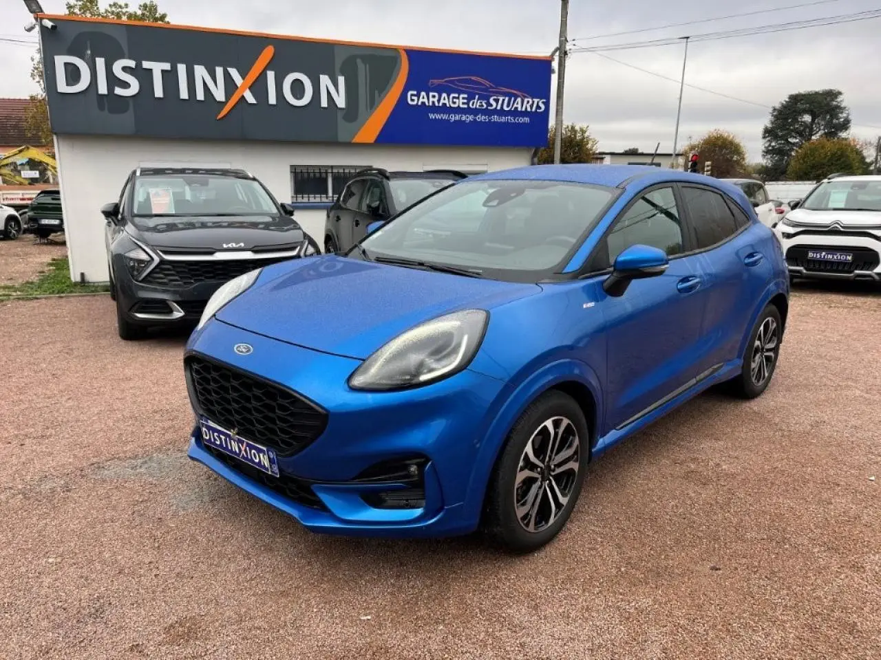 Ford Puma bleu 3/4 avant droit, avec jantes alliage noires et vitres arrière surteintées, sur parking extérieur.