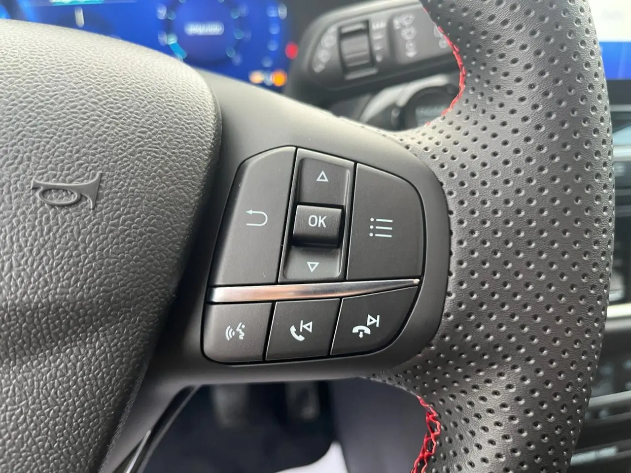 Gros plan sur les commandes multifonctions à droite du volant perforé avec surpiqûres rouges du Ford Puma bleu 2022.