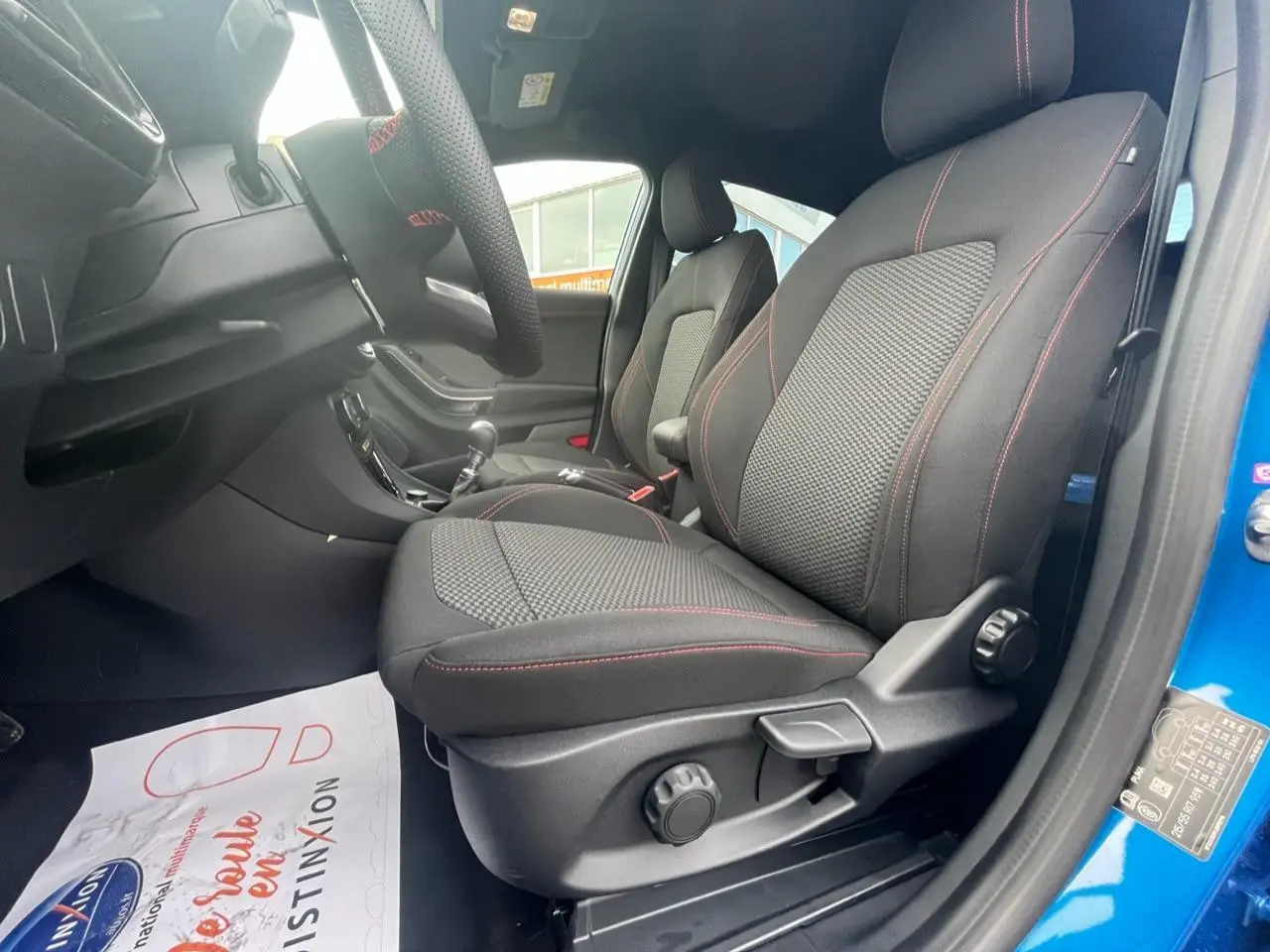 Vue intérieure côté conducteur du Ford Puma bleu 2022, sièges tissu noir avec surpiqûres rouges et volant sport.
