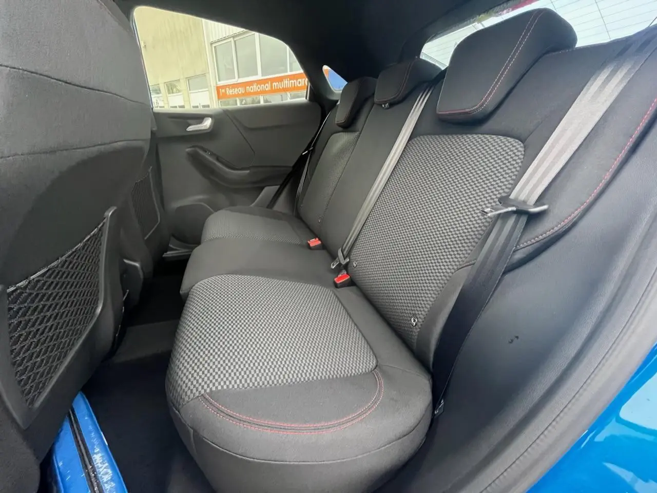 Vue intérieure côté droit sur la banquette arrière noire avec surpiqûres rouges du Ford Puma bleu 2022.