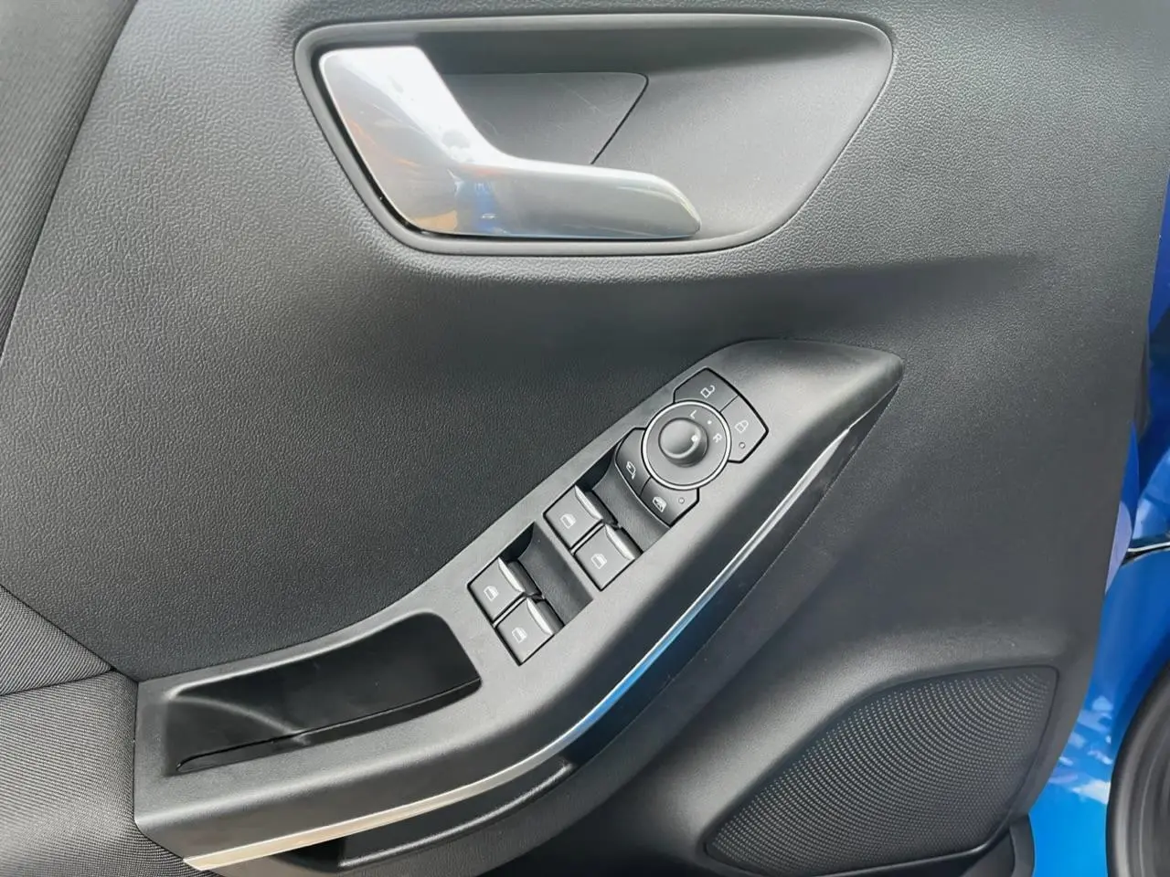 Gros plan sur la porte avant gauche du Ford Puma bleu, montrant les commandes des vitres et le haut-parleur intégré.