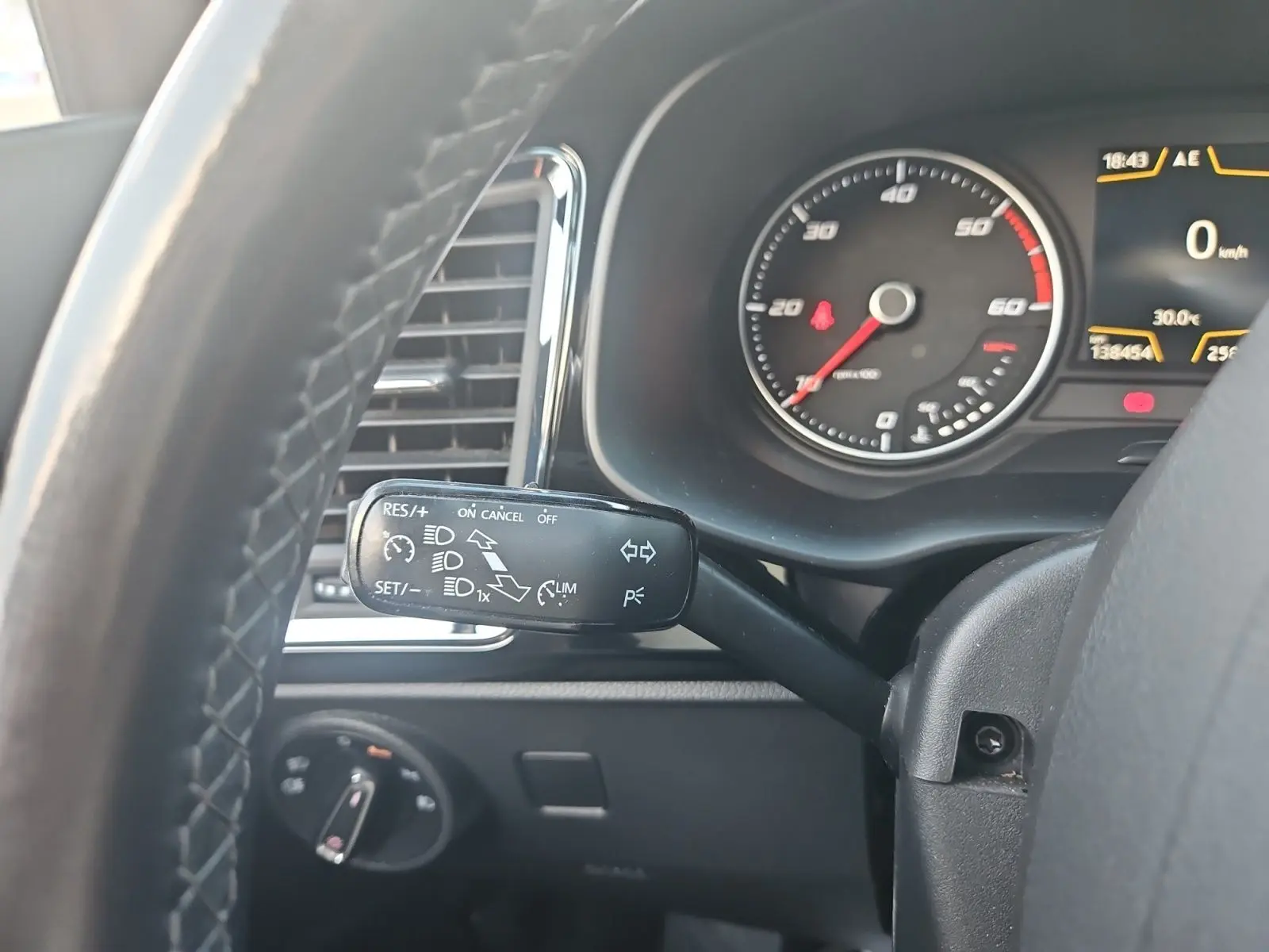 Gros plan sur le commodo gauche du volant en cuir du SEAT Ateca blanc, avec tableau de bord et compteur visible.
