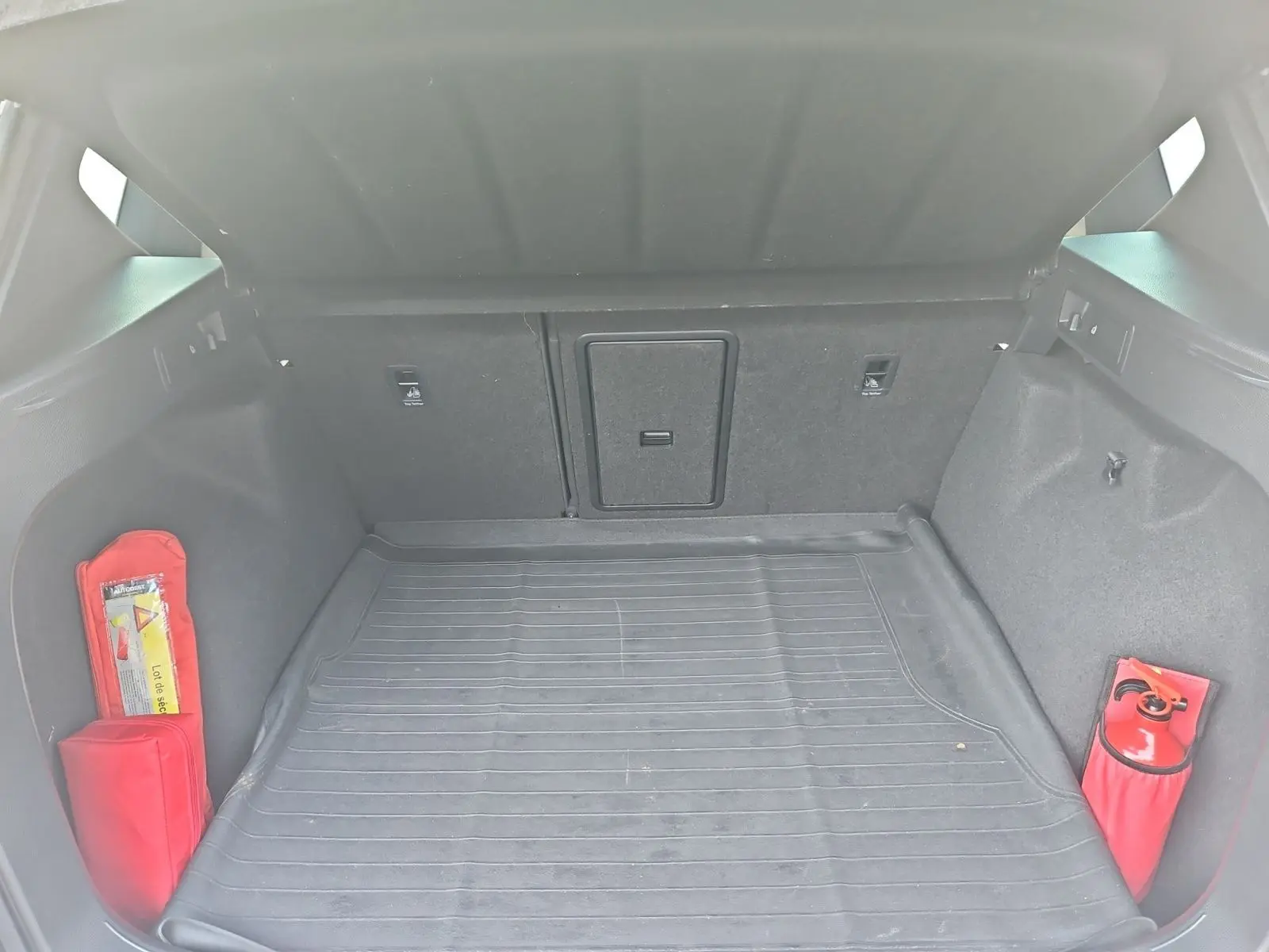 Coffre ouvert d'un SEAT Ateca blanc, vue intérieure montrant tapis de sol et équipements de sécurité rouges.