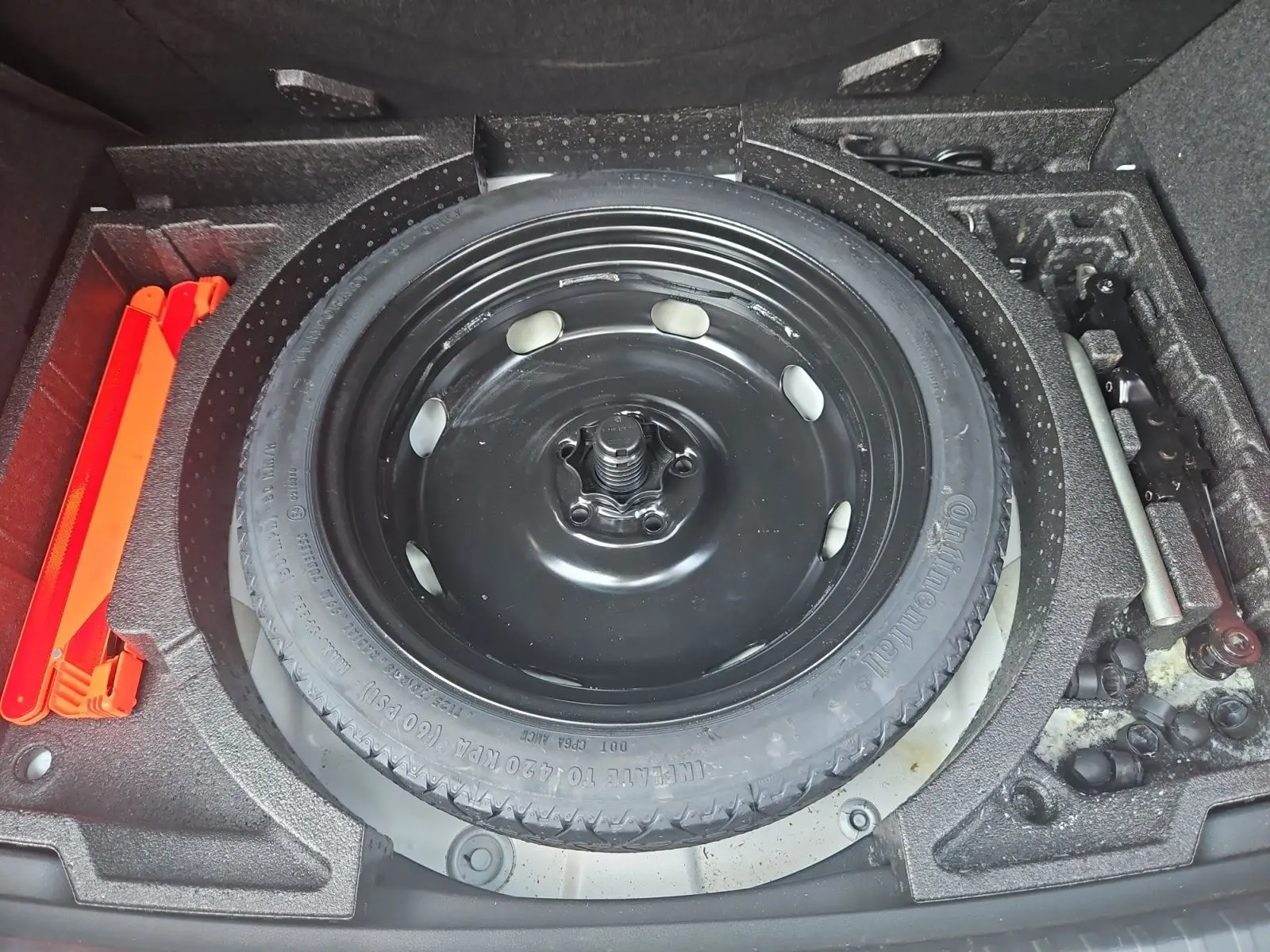 Vue plongeante sur la roue de secours galette noire et les outils de bord dans le coffre d'un SEAT Ateca blanc.