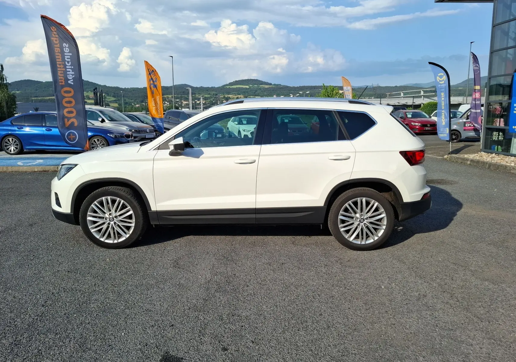 Vue de profil côté gauche d’un SEAT Ateca blanc avec jantes alliage 18 pouces, barres de toit et vitres teintées.