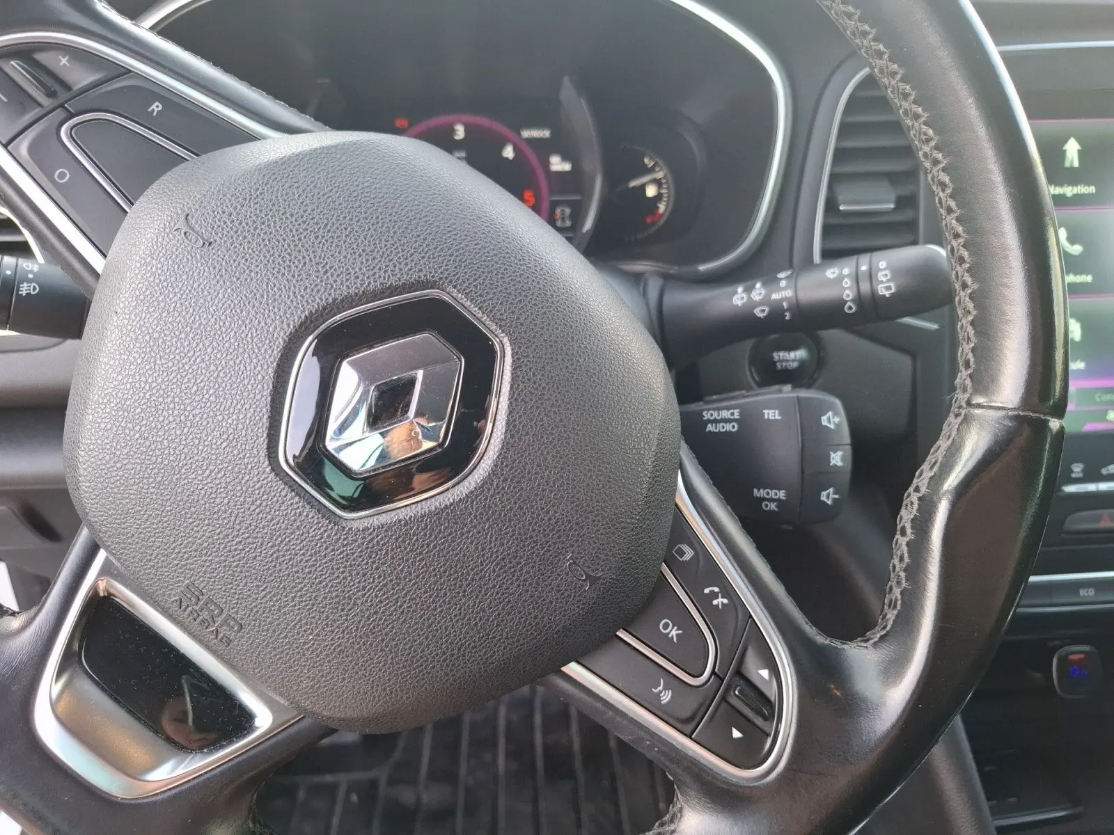Vue rapprochée du volant noir de la Renault Mégane 1.6 DCI 130 Energy Intens avec commandes intégrées et tableau de bord en arrière-plan.