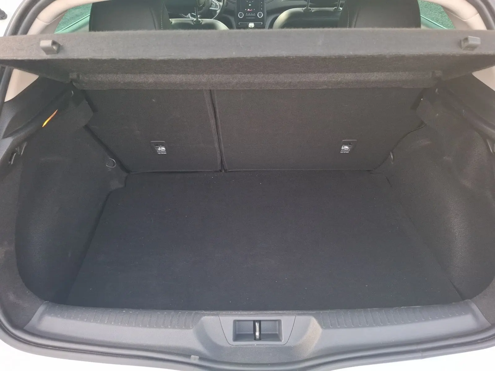 Coffre ouvert vu de l'arrière d'une Renault Mégane blanche, espace de chargement vide et habillage intérieur noir.