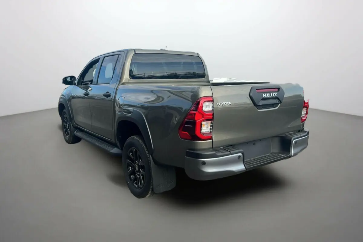 Toyota Hilux 4x4 2025 en bronze impérial, vue 3/4 arrière côté gauche avec benne et jantes noires.