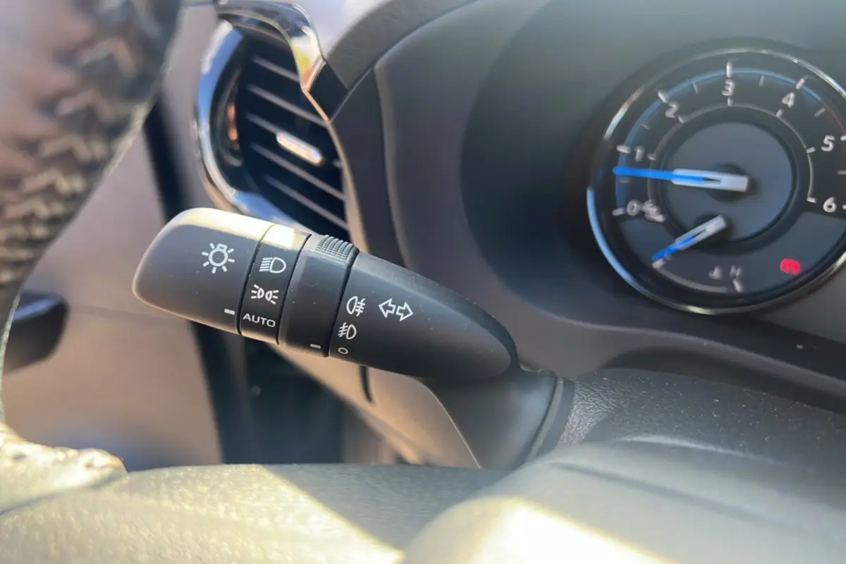 Gros plan sur la commande des phares à gauche du volant du Toyota Hilux 2025 gris atlas, tableau de bord en arrière-plan.