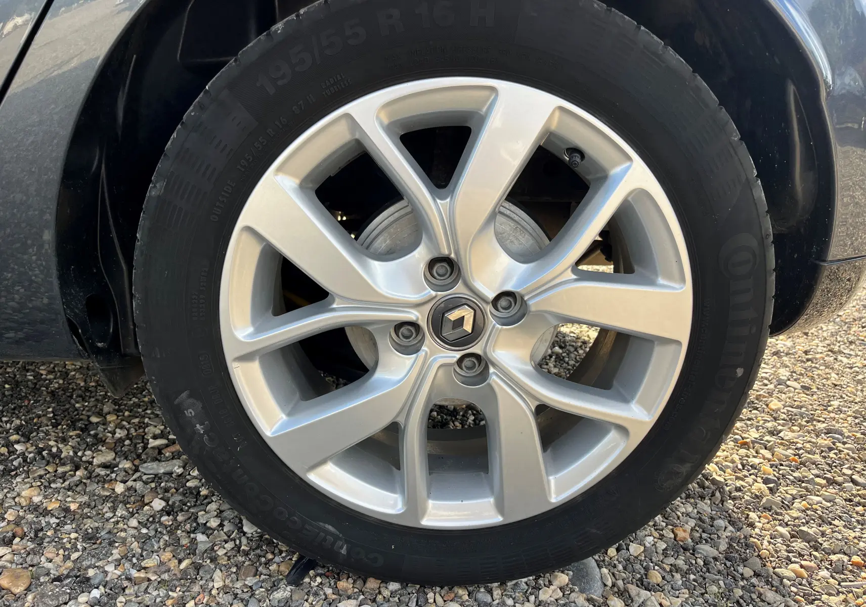 Gros plan sur la jante alliage argentée avec logo Renault au centre d'une Renault Clio IV diesel bleue.