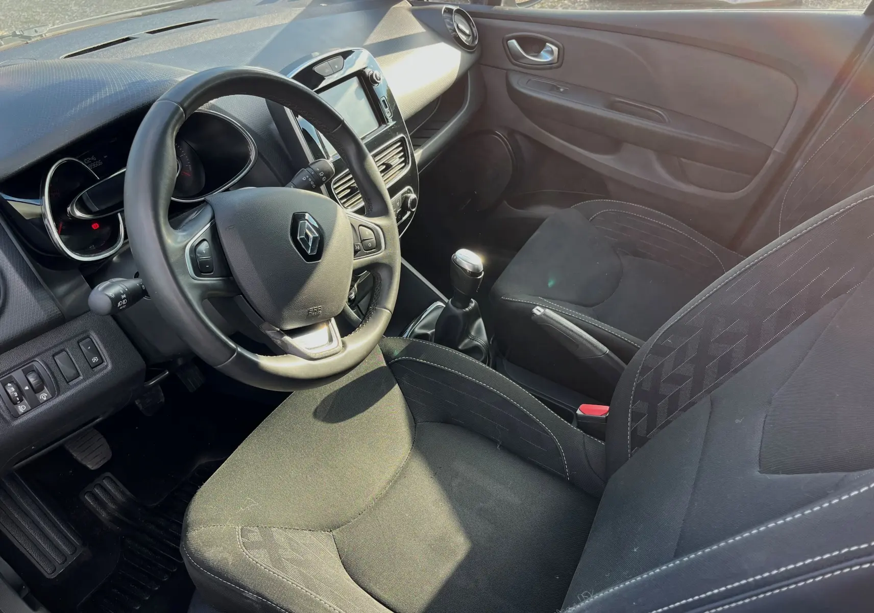 Intérieur noir de la Renault Clio IV 2019, vue côté conducteur montrant volant, tableau de bord et siège tissu.