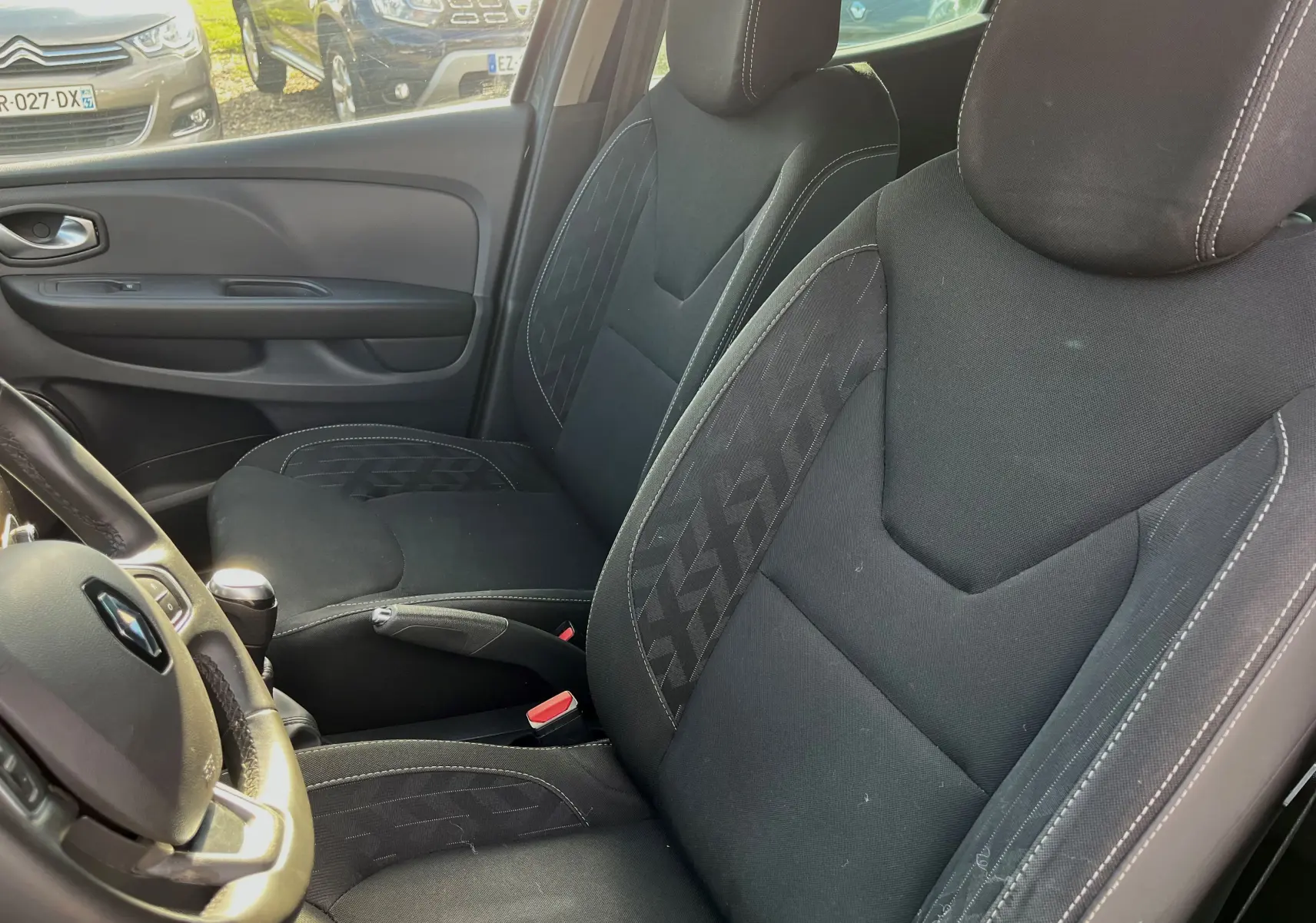 Vue intérieure sur les sièges avant en tissu noir et volant de la Renault Clio IV diesel 2019, côté gauche visible.