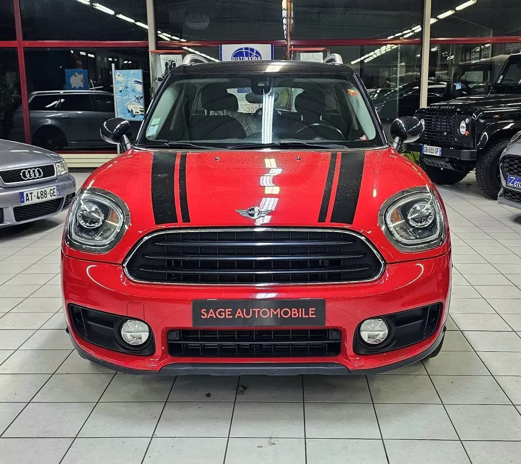 Vue avant d'une MINI Cooper Countryman rouge avec bandes noires sur le capot, en intérieur showroom.