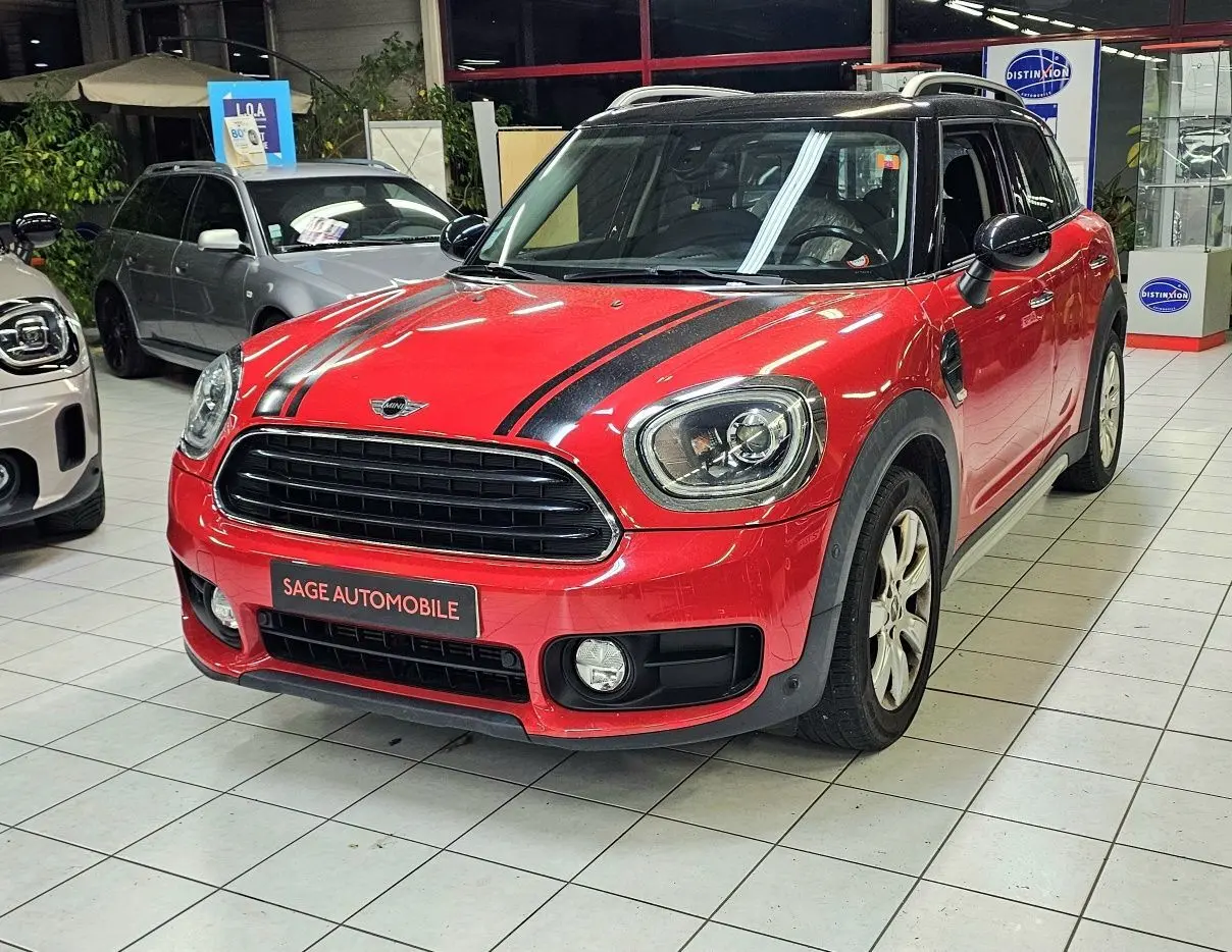 Vue 3/4 avant d'une MINI Cooper Countryman rouge avec bandes noires sur le capot, en showroom intérieur.