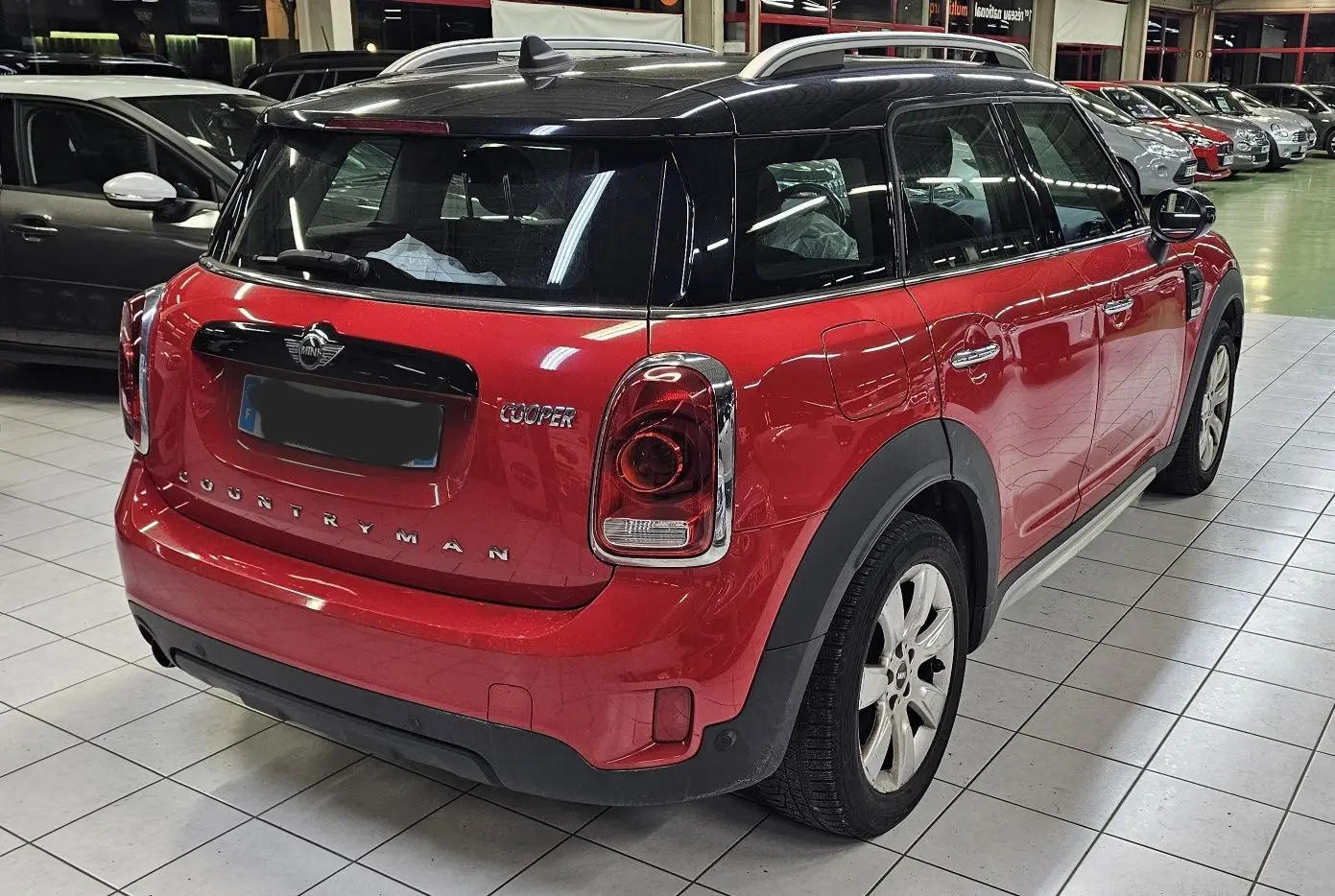 Vue 3/4 arrière droite d'une MINI Cooper Countryman rouge avec toit noir, dans un showroom intérieur.