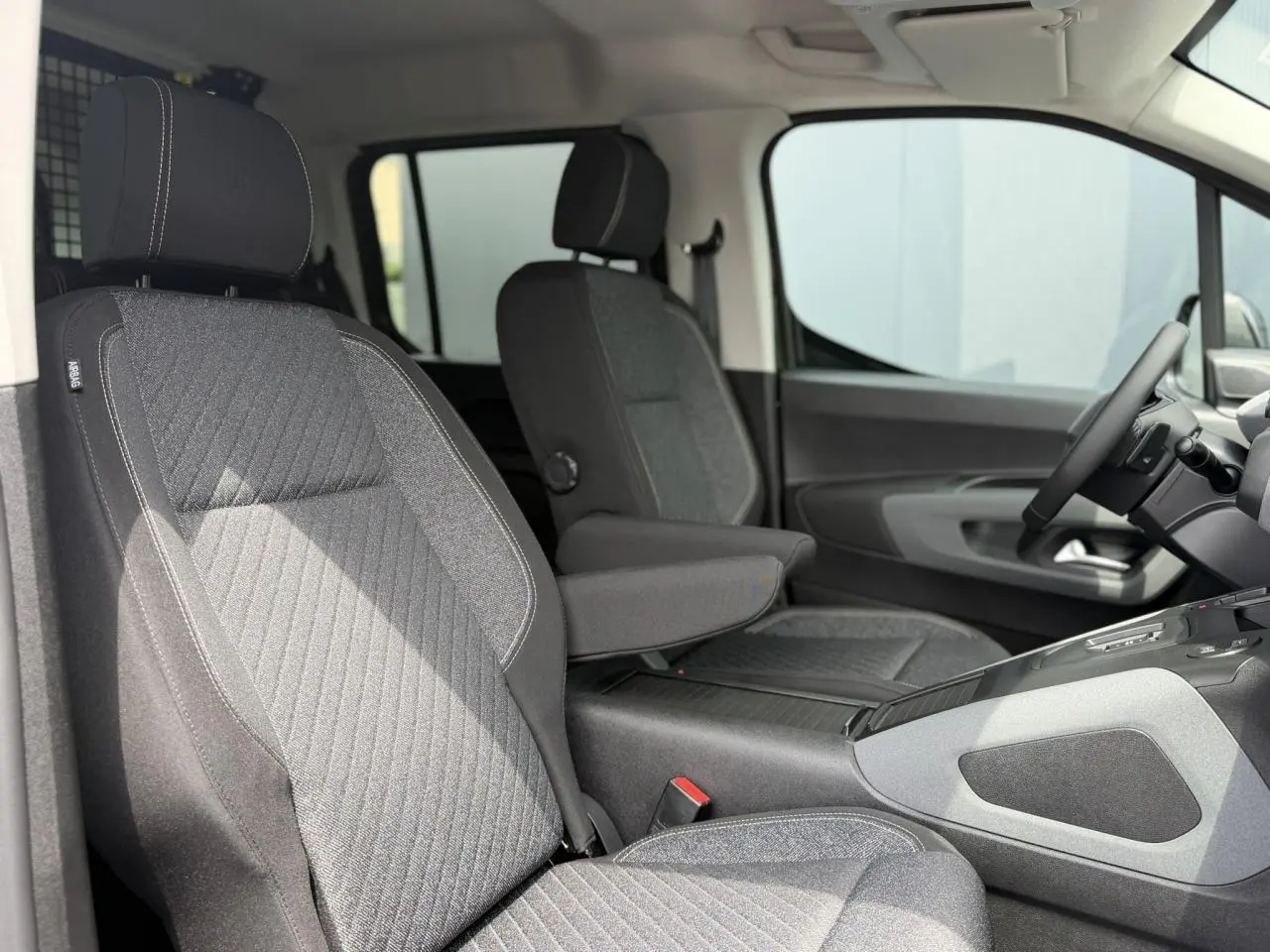 Vue intérieure côté droit du Peugeot Rifter 2026, sièges tissu gris avec accoudoir central déployé.