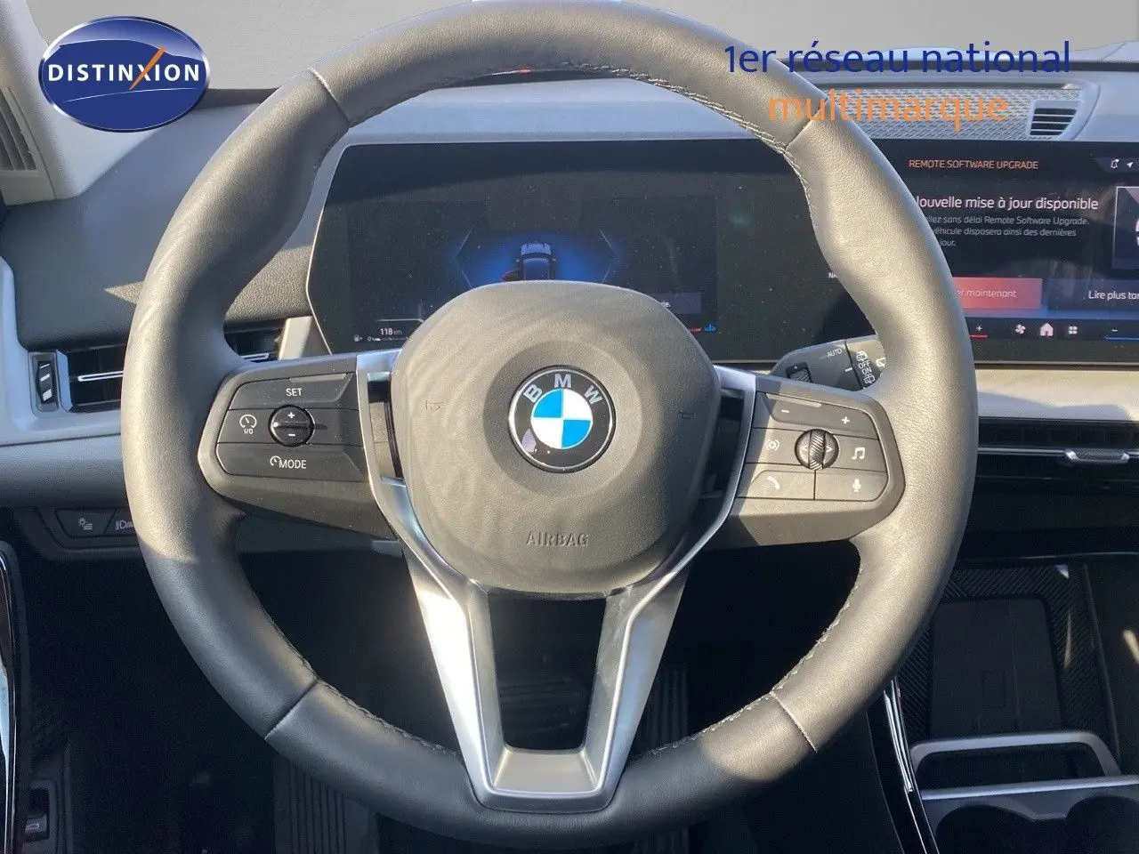 Volant en cuir noir avec logo BMW au centre, tableau de bord numérique et écran tactile du BMW X1 18I 2024 visible de face.